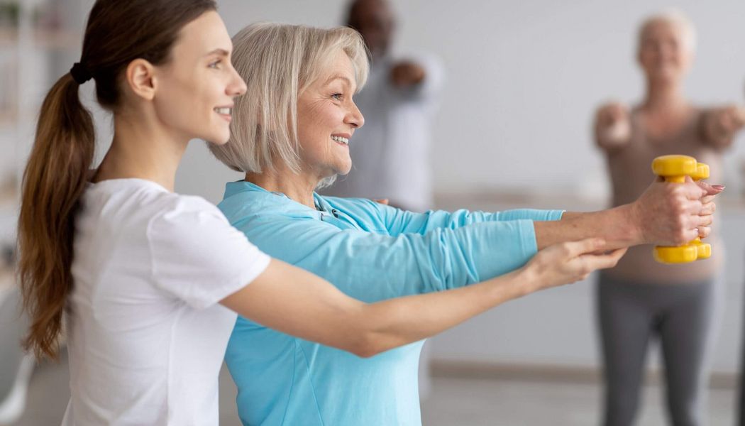 Eine Frau hilft einer älteren Dame beim Hanteltraining in einem Fitnesskurs.