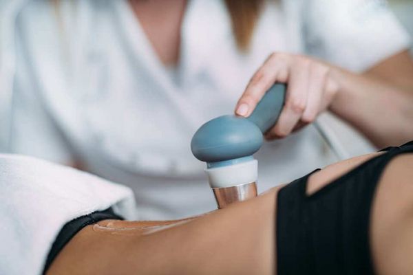 Eine Person führt eine Ultraschalltherapie mit einem Handgerät auf einem Knie durch.