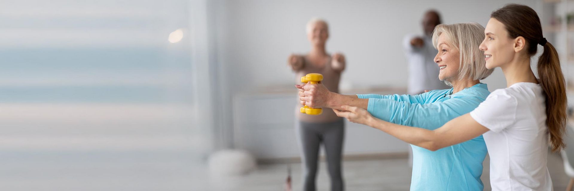 Eine Frau hilft einer älteren Frau beim Hanteltraining in einem Fitnessstudio.
