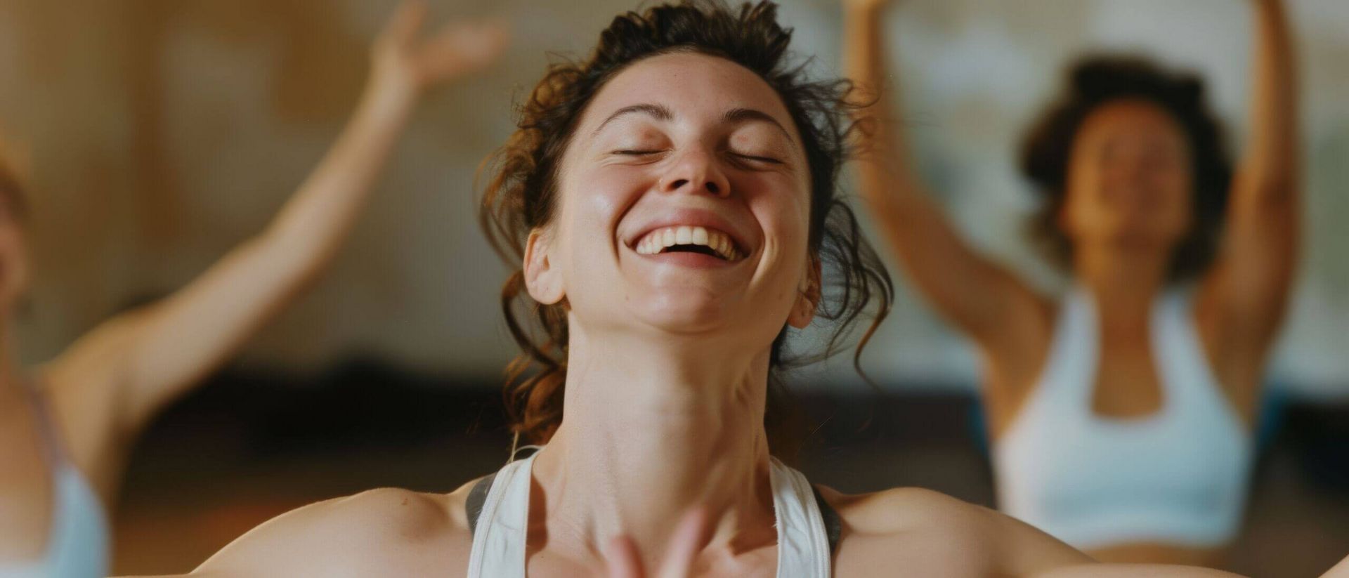 Eine junge Frau strahlt vor Freude in einer energetischen Yogastunde, umgeben von anderen Praktizierenden im Studio.