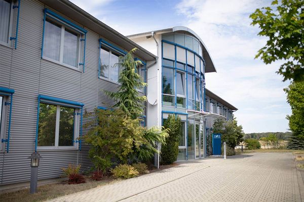 Das moderne Gebäude von PhysioFitPlus in Harbke steht umgeben von grüner Bepflanzung unter einem klaren blauen Himmel.