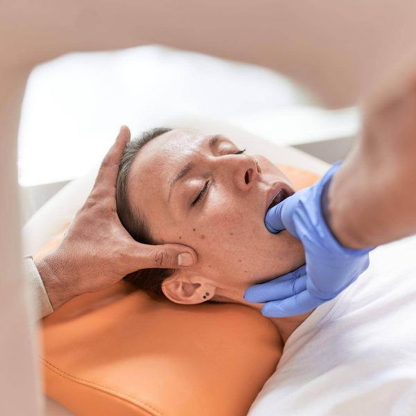 Eine Person erhält eine CMD-Therapie mit oraler Technik, während sie entspannt auf einem orangefarbenen Kissen liegt.